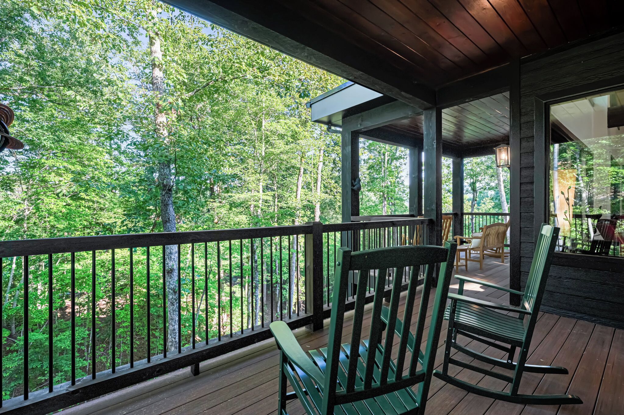 A wooden deck with a railing, green rocking chairs, and a view of a forest.