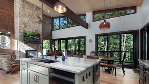 A spacious kitchen with a large island, stone wall, and large windows offering views of the outdoors.