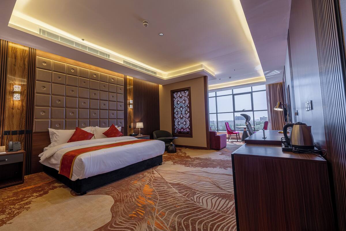 A modern hotel room with a large bed, a desk, and a view of the city.
