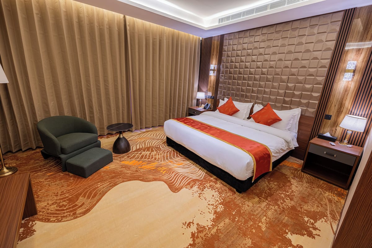 A hotel room with a large bed, a chair, a small table, and a nightstand.