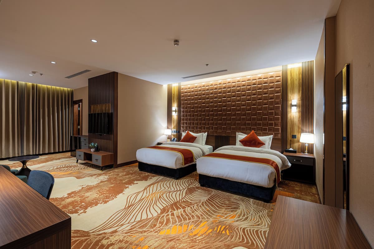 A hotel room with two beds, a desk, a chair, a lamp, and a patterned carpet.