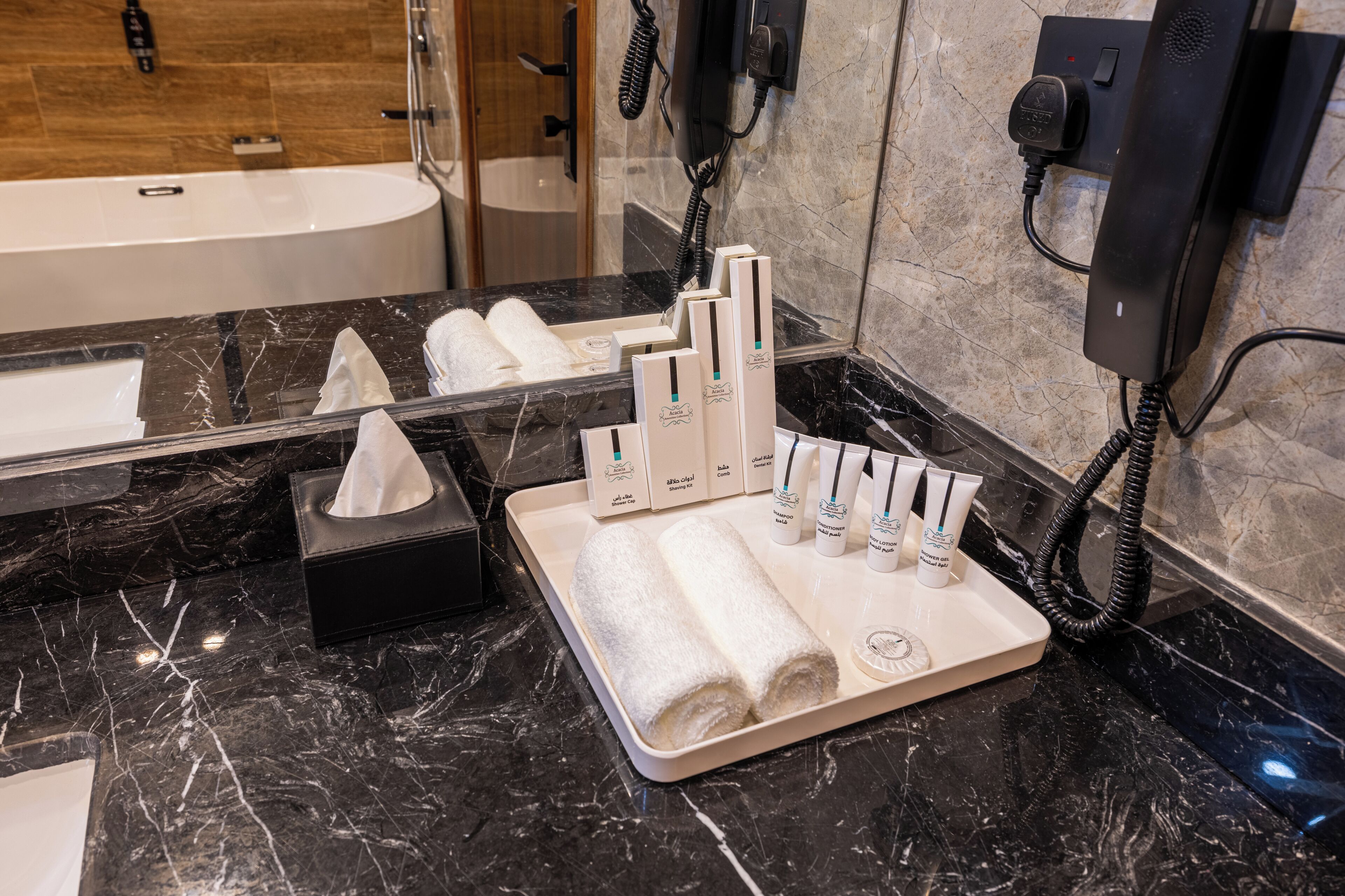 Un baño con encimera de mármol, perchero, caja de pañuelos y un juego de artículos de aseo que incluye cepillo de dientes, pasta de dientes y champú.