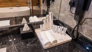 Un baño con encimera de mármol, perchero, caja de pañuelos y un juego de artículos de aseo que incluye cepillo de dientes, pasta de dientes y champú.