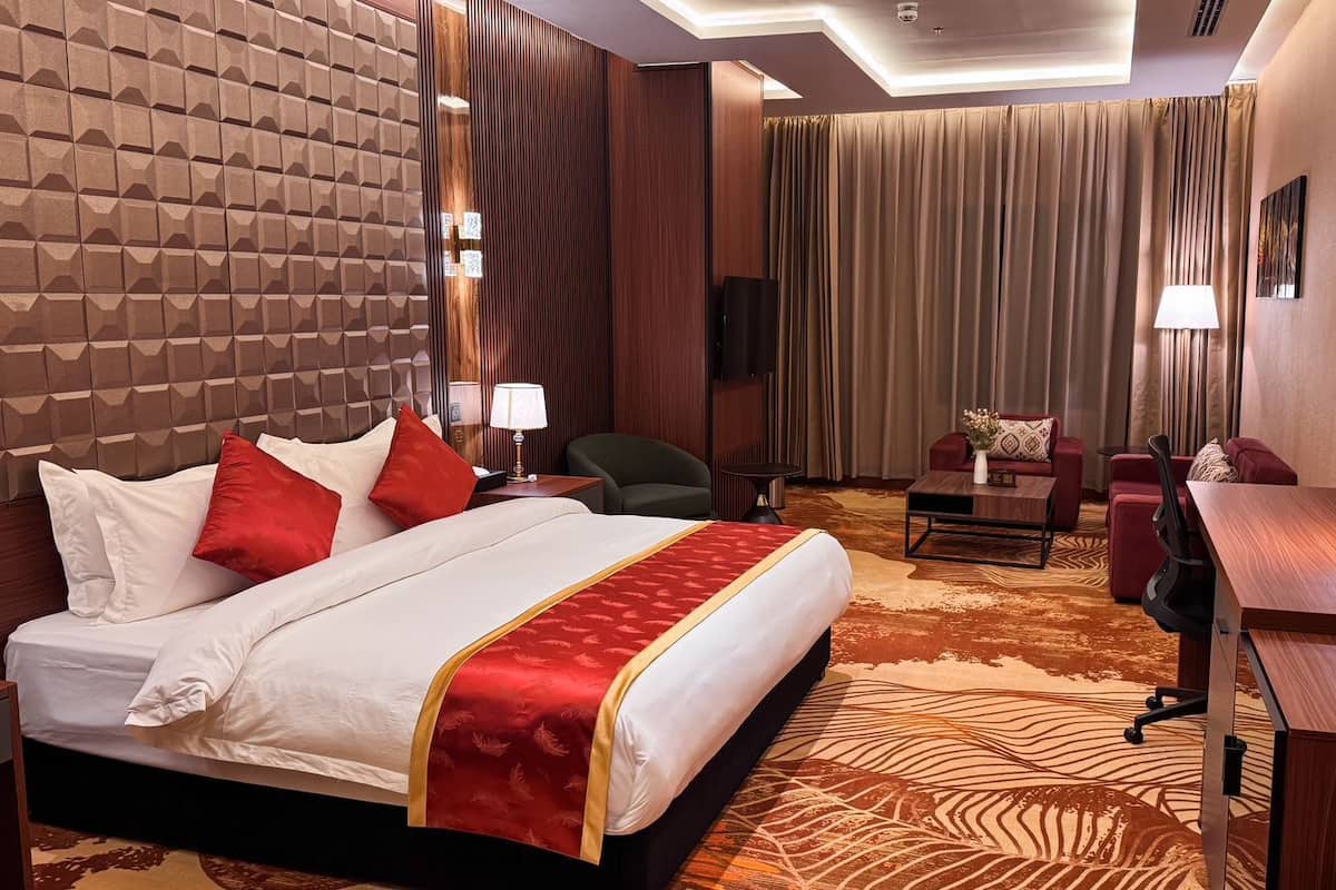 A hotel room with a large bed, a desk, a chair, a sofa, and a TV.