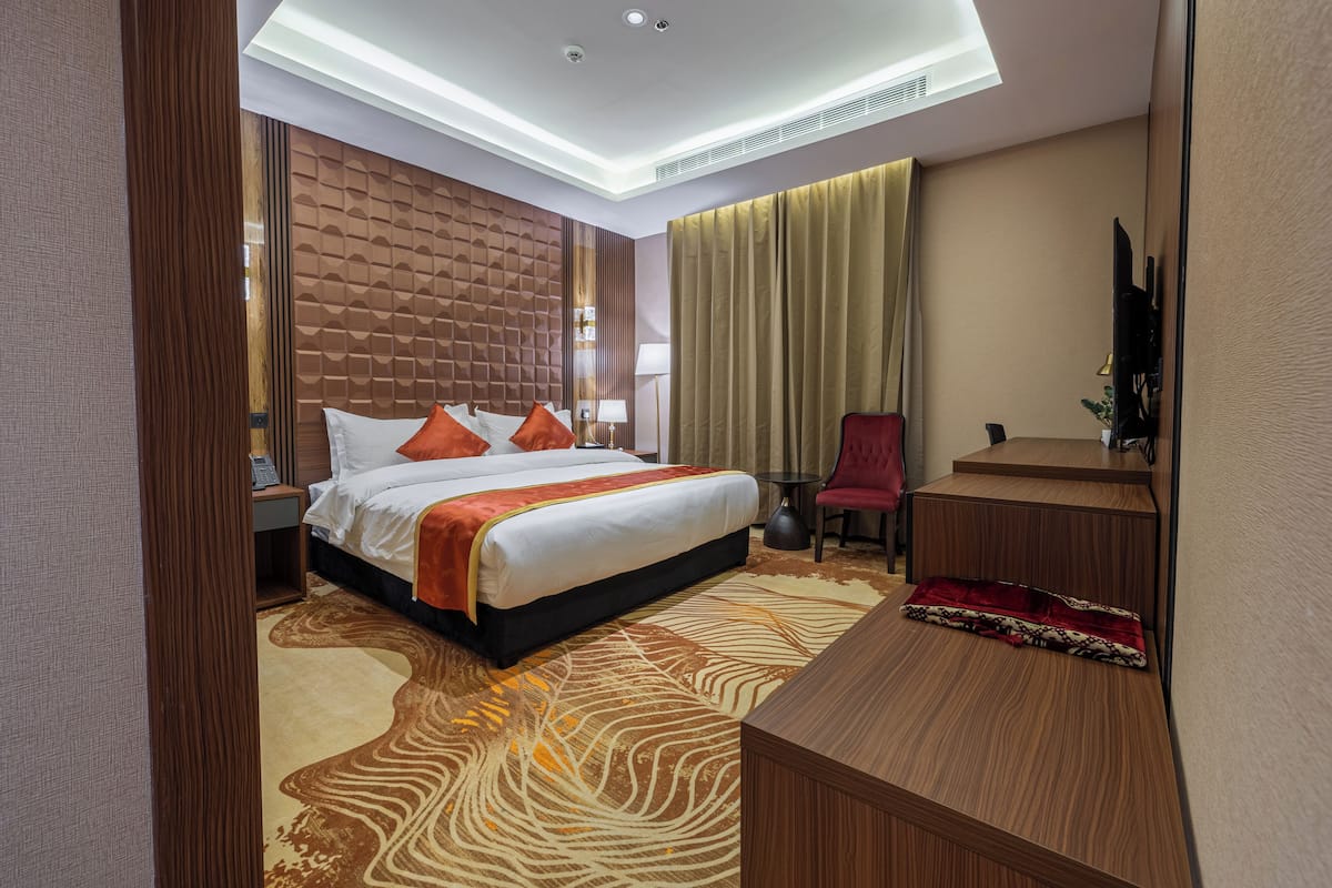A modern hotel room with a large bed, a desk, a chair, and a television.