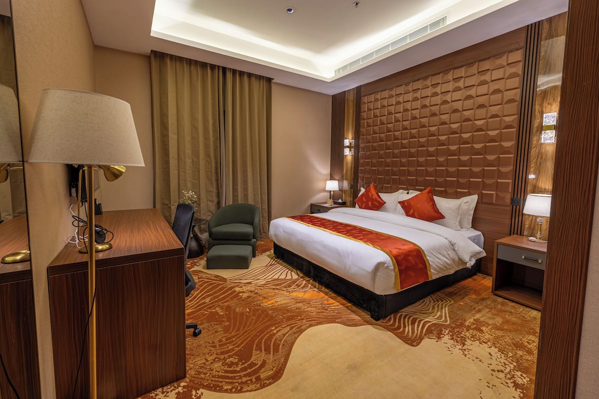 A hotel room with a large bed, a desk, a chair, and a lamp.