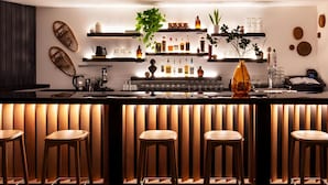 A modern bar area with wooden slats, bar stools, shelves with bottles, and decorative items.