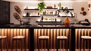 A modern bar area with wooden slats, bar stools, shelves with bottles, and decorative items. - Deluxe King | Tälta Lodge, a Bluebird by Lark | with Bike Rentals & Free Coffee (Stowe)