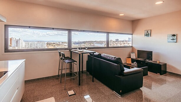 Ein modernes Hotelzimmer mit Blick auf die Stadt, einer Couch, einem kleinen Tisch und einem Fernseher.