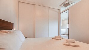 Ein Hotelzimmer mit einem großen Bett, einem Holz-Kopfteil, einem Schiebetürenschrank und einem durch eine geöffnete Tür einsehbaren Badezimmer.