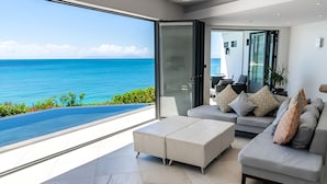 Ein modernes Wohnzimmer mit einem großen Glastür, das auf einen Balkon mit Blick auf das klare, blaue Meer führt.