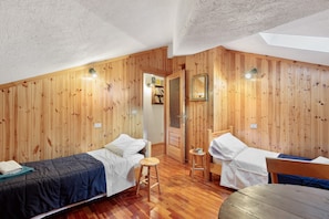 A room with wooden walls, two beds, a small stool, and a table.