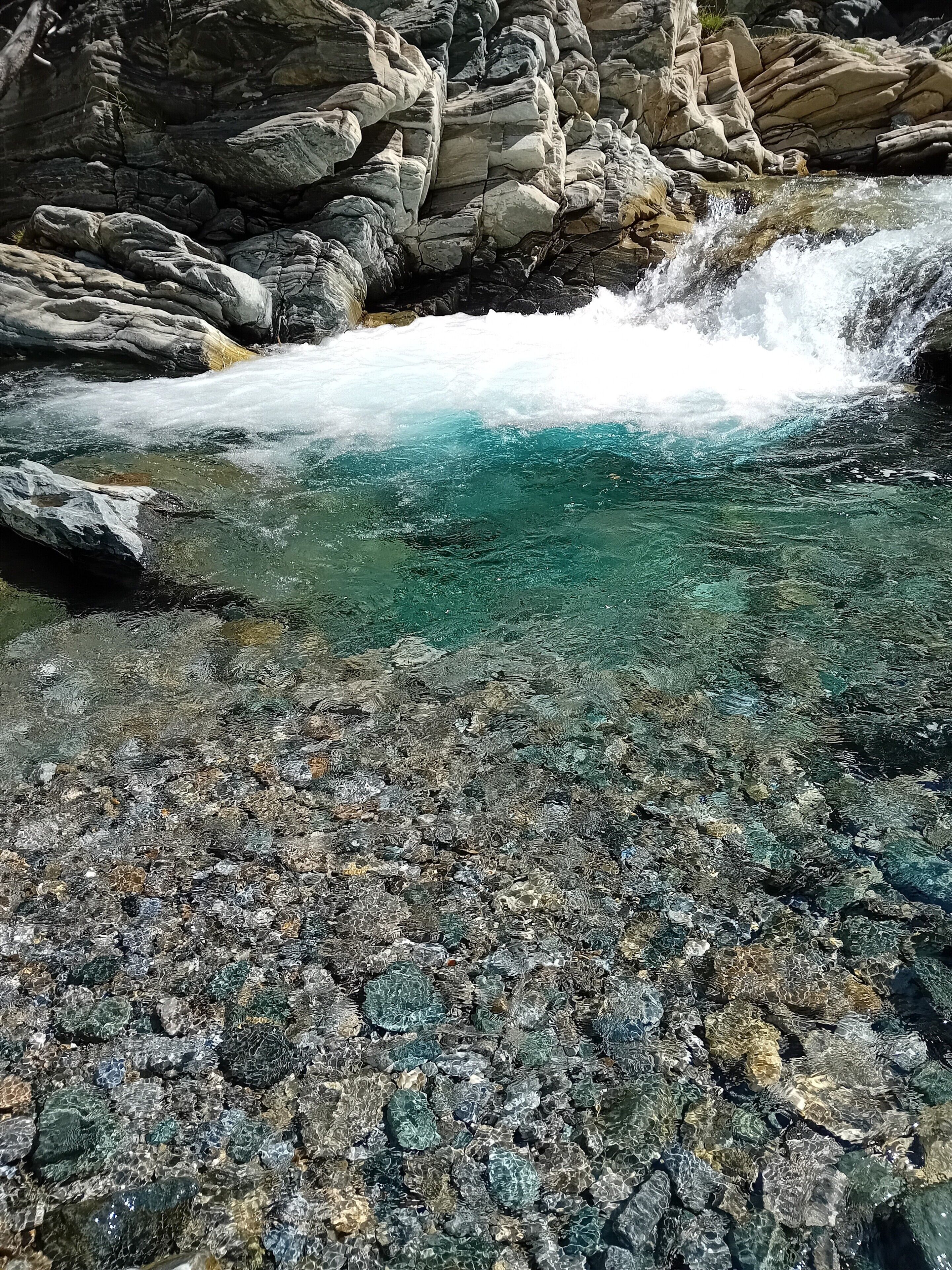 A rocky stream with clear water, surrounded by large boulders and a rugged landscape.