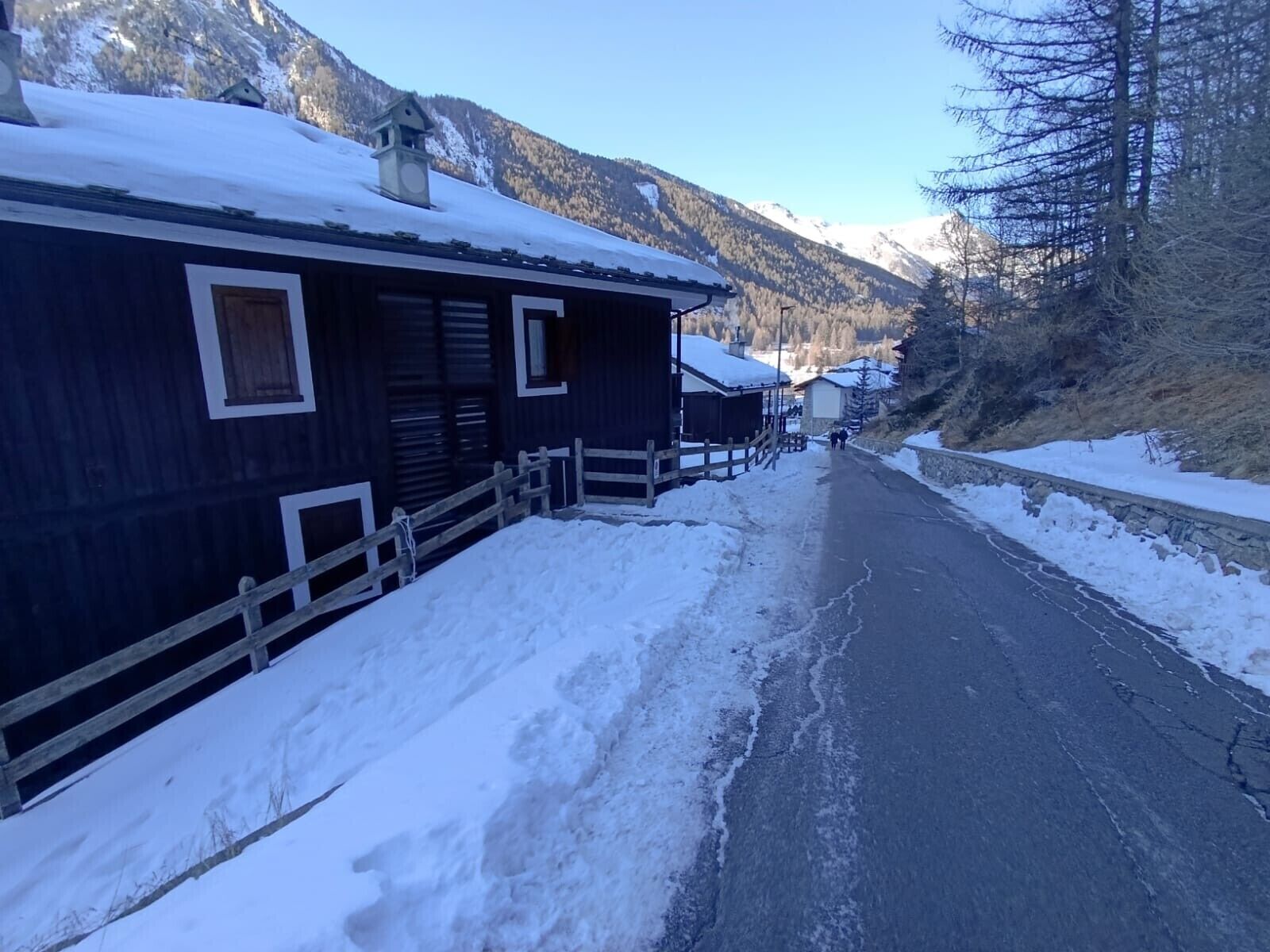 A snow-covered street with wooden buildings, a clock tower, and mountains in the background.