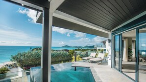 A modern outdoor pool area with clear blue water, lounge chairs, and a view of the ocean and distant mountains. - 2BR Beachfront Villa | Direct Access | Antigua Views (Urlings)