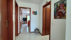 A hallway with wooden doors, a tiled floor, and a television in the background.