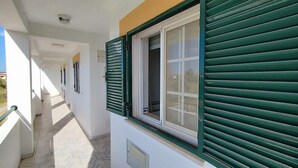 Un couloir avec une fenêtre dotée de volets verts, une porte blanche et un sol carrelé.