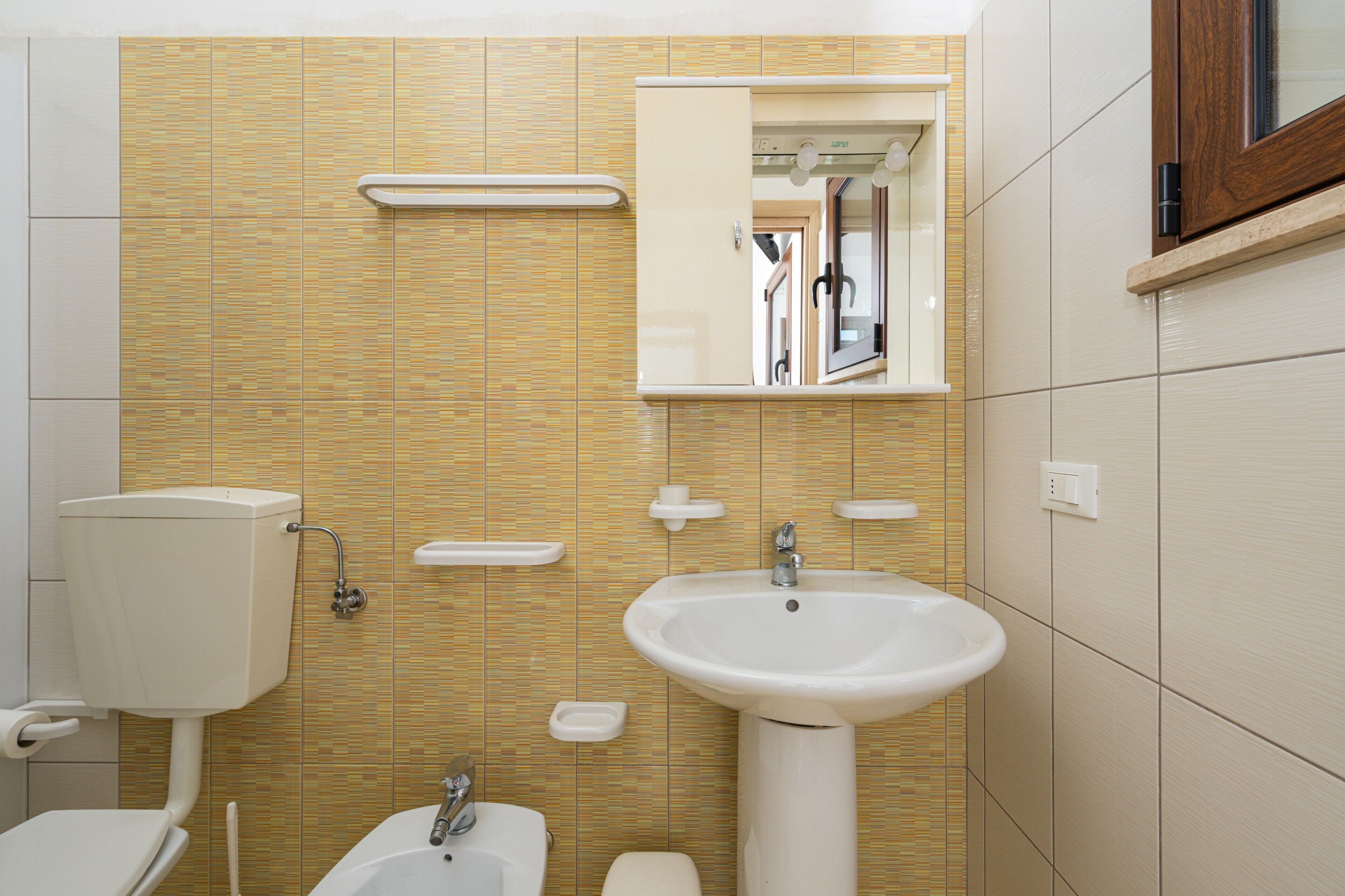Un bagno con WC, lavandino, specchio e pareti piastrellate.