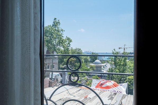 Une vue depuis une fenêtre ornée d’un garde-corps en métal, donnant sur un paysage urbain avec des bâtiments, des arbres et une grue de construction.