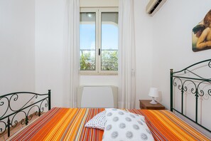 Une chambre à coucher avec un lit, une table de chevet, une lampe, une fenêtre avec des rideaux et un tableau au mur.