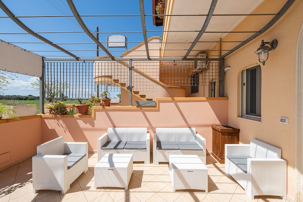 Un espace extérieur aménagé, abrité et doté de mobilier en osier, d’un escalier et offrant une vue sur la campagne.