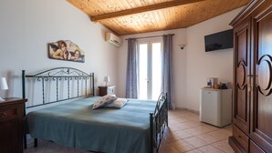 A bedroom with a bed, a wooden ceiling, a wall-mounted TV, a small refrigerator, and a cabinet.