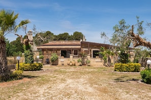 A traditional building with a tiled roof, surrounded by well-maintained gardens and a clear sky.