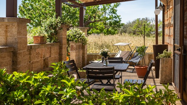 Eine Terrasse im Freien mit einer Pergola, Steinmauern, Kübelpflanzen und einem Tisch mit Stühlen.
