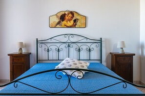 Un lit recouvert d’une couvre-lit bleue, une tête de lit décorative, deux tables de chevet avec des lampes et un tableau encadré accroché au mur.