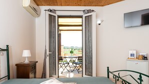 A bedroom with a bed, a nightstand with a lamp, a dresser, a TV, and a balcony with a table and chairs.