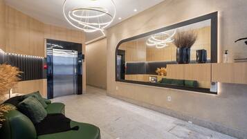A modern lobby with a green sofa, a large mirror, and a ceiling light fixture.