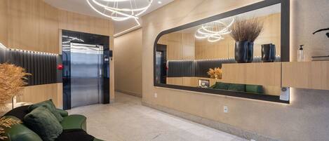 A modern lobby with a green sofa, a large mirror, and a ceiling light fixture.