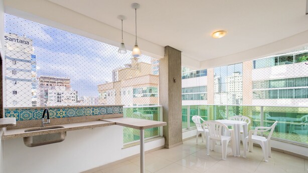 A modern kitchen with a tiled backsplash, a sink, and a dining area with white chairs and a table. - 450m Beach Apt - Bbq, 3 Suites Tah0602 (Itapema)