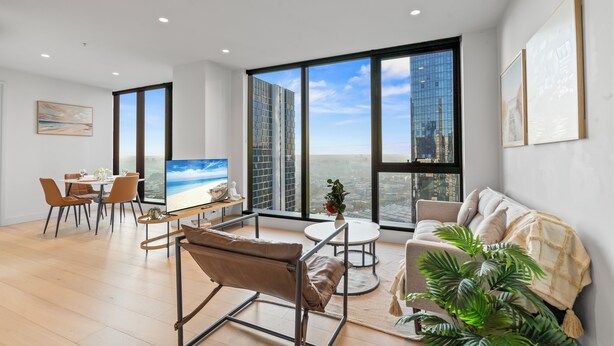 Ein modernes Wohnzimmer mit großem Fernseher, einem Essbereich und Blick auf die Stadt durch hohe Fenster.