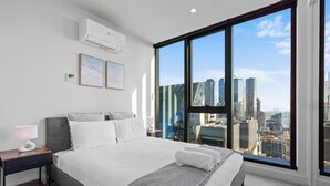 Ein modernes Schlafzimmer mit einem großen Bett, einem Nachttisch, einer Lampe und Blick auf den Stadtgürtel durch raumhohe Fenster.