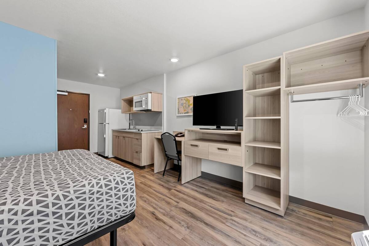 A compact room with a bed, a desk, a chair, a TV, a wardrobe, and a microwave.