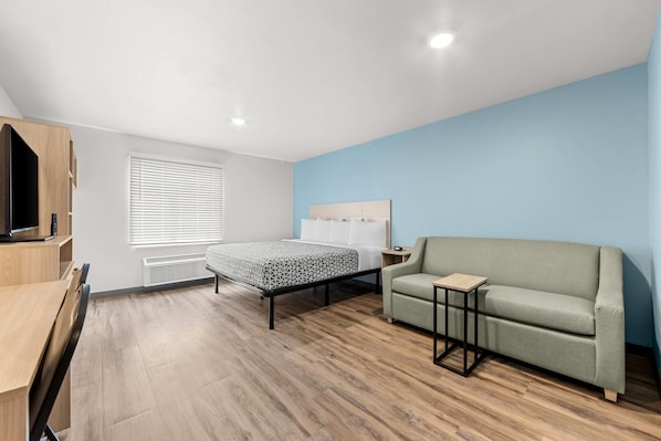 A modern bedroom with a bed, a sofa, a TV, and a desk. - WoodSpring Suites Oak Ridge Knoxville (Oak Ridge)