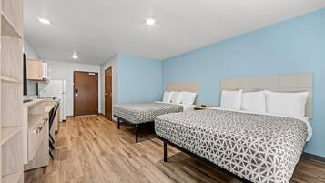 A hotel room with two beds, a kitchenette, and a wooden floor.
