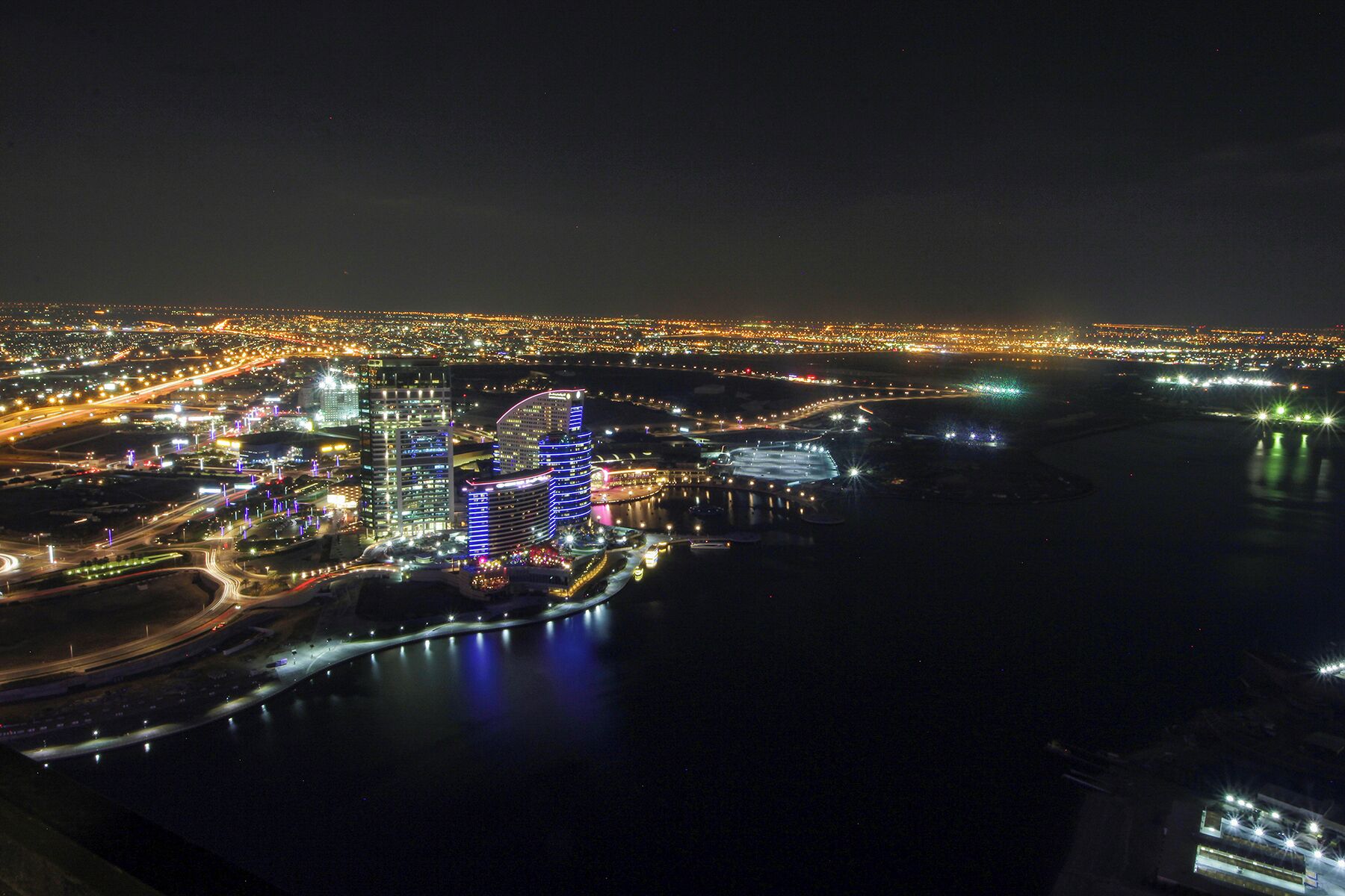 A nighttime aerial view of a cityscape with illuminated buildings and a waterfront.
