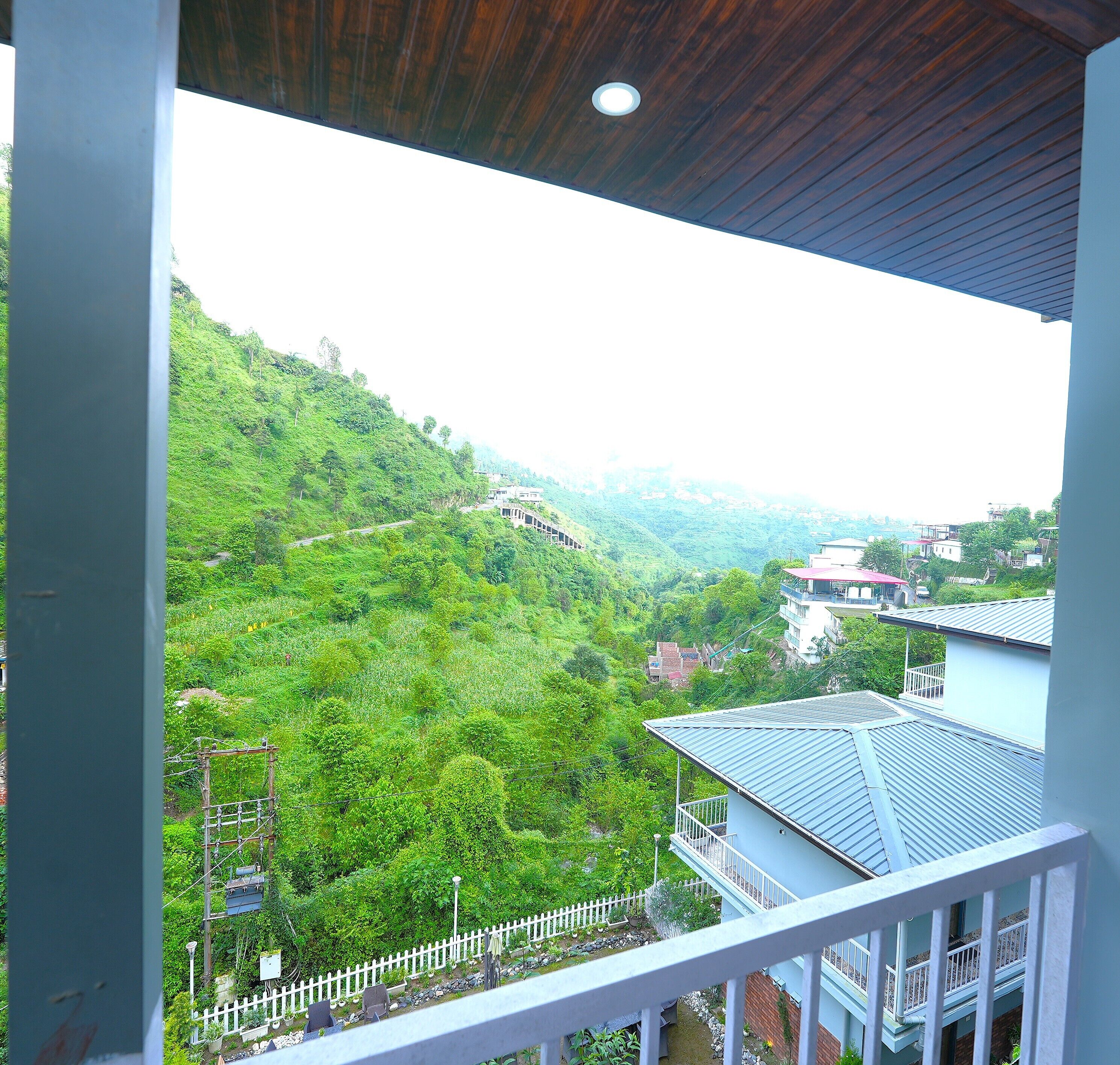 Un balcon donnant sur une colline verdoyante et quelques bâtiments visibles au loin.