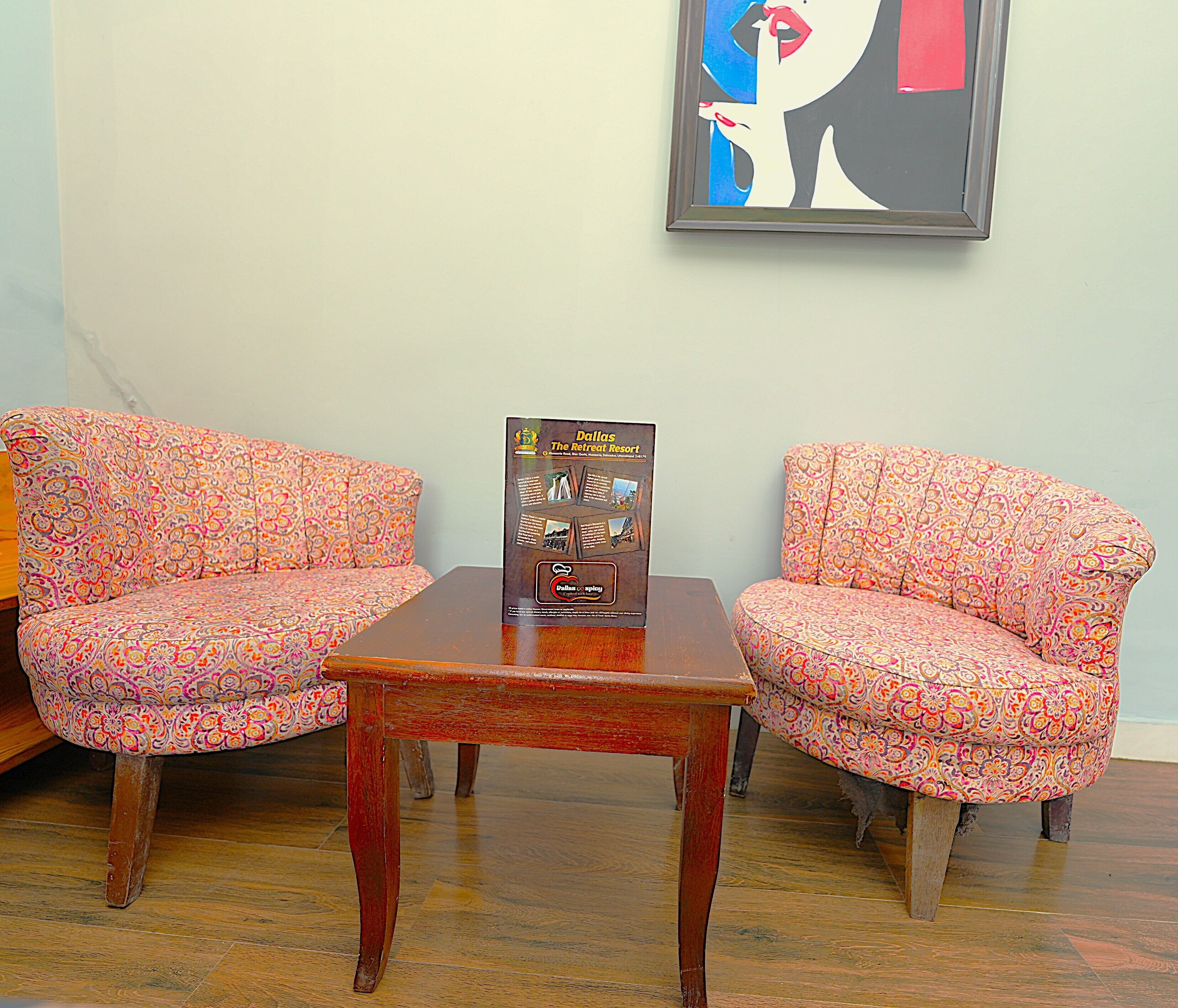 Dos sillones estampados y una pequeña mesa de madera en una habitación con un cuadro abstracto enmarcado en la pared.