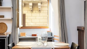 A dining area with a table set for two, a window with a view of a brick wall, and striped curtains. - Rental in Rome Pantheon Apartment (Rome)