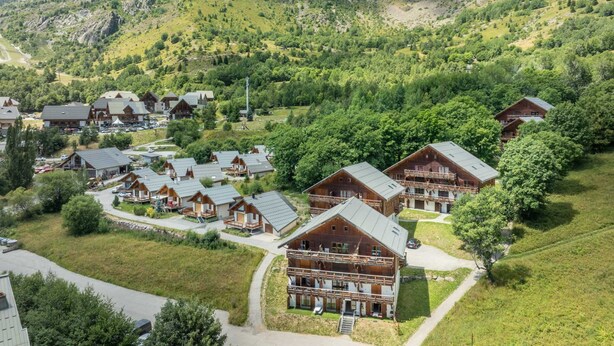 A cluster of wooden cabins with multiple stories and balconies, surrounded by lush greenery and a mountainous backdrop. - Mountain Apartment in Saint-sorlin (Saint-Sorlin-d'Arves)