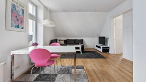 A modern living room with a white desk, pink chairs, a grey rug, a black sofa, and a TV stand. - Apartment '3' Villa Elysium (Heide)
