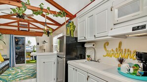 Una cocina con armarios blancos, un refrigerador negro y un ventilador de techo. En la pared, hay un letrero que dice "Sunshine".
