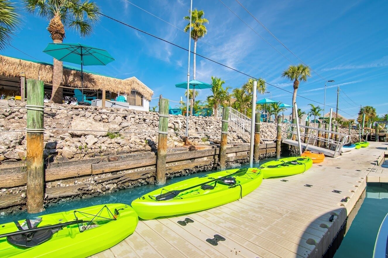A dock with kayaks, a pool, and a thatched-roof structure.