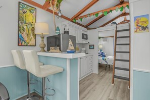 A kitchen with a bar area, a microwave, and a refrigerator. There is a ladder leaning against the wall and a painting of a parrot on the wall. - Cozy Boathouse in Fort Myers Beach (Fort Myers Beach)