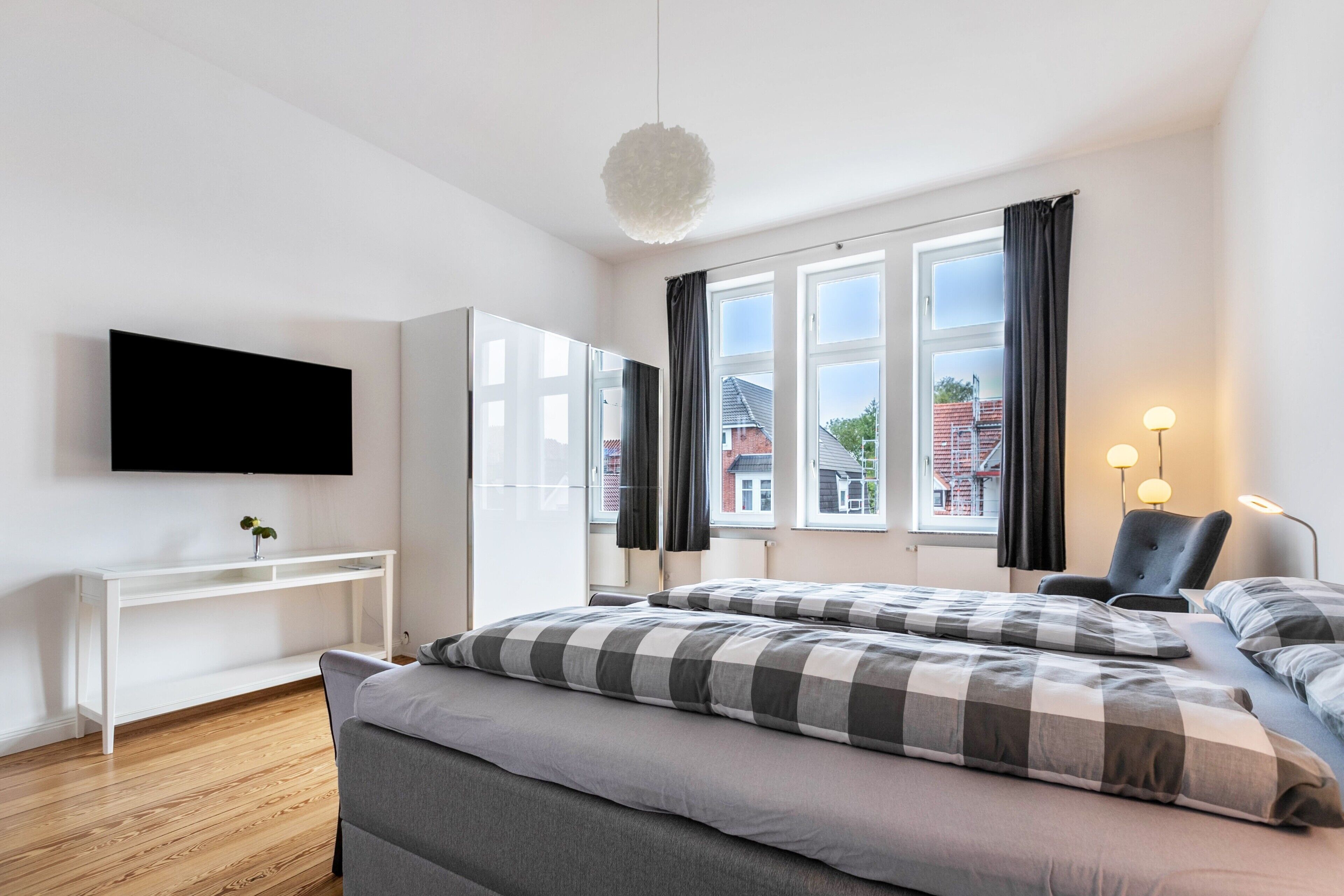 Una camera d'albergo moderna con un letto, una TV, una scrivania e una finestra con tende.