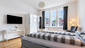 A modern hotel room with a bed, a TV, a desk, and a window with curtains.