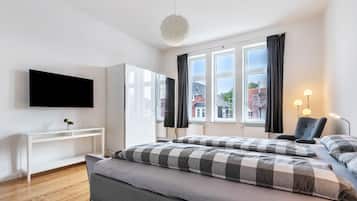 Una camera d'albergo moderna con un letto, una TV, una scrivania e una finestra con tende.